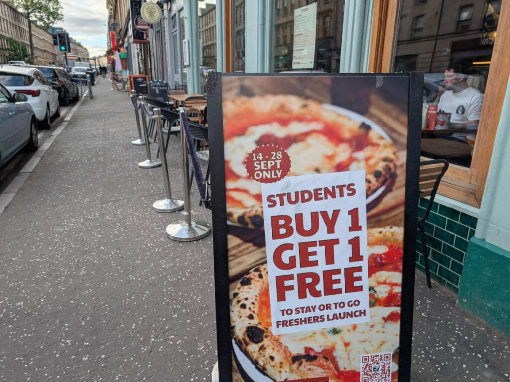A buy 1 take 1 for students signage outside a pizza shop