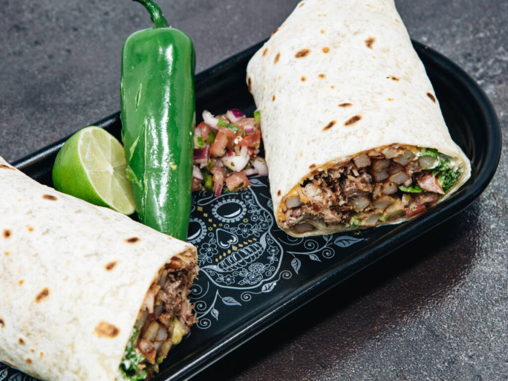 A small plate with sliced in half burrito, a chili pepper, and sliced lime