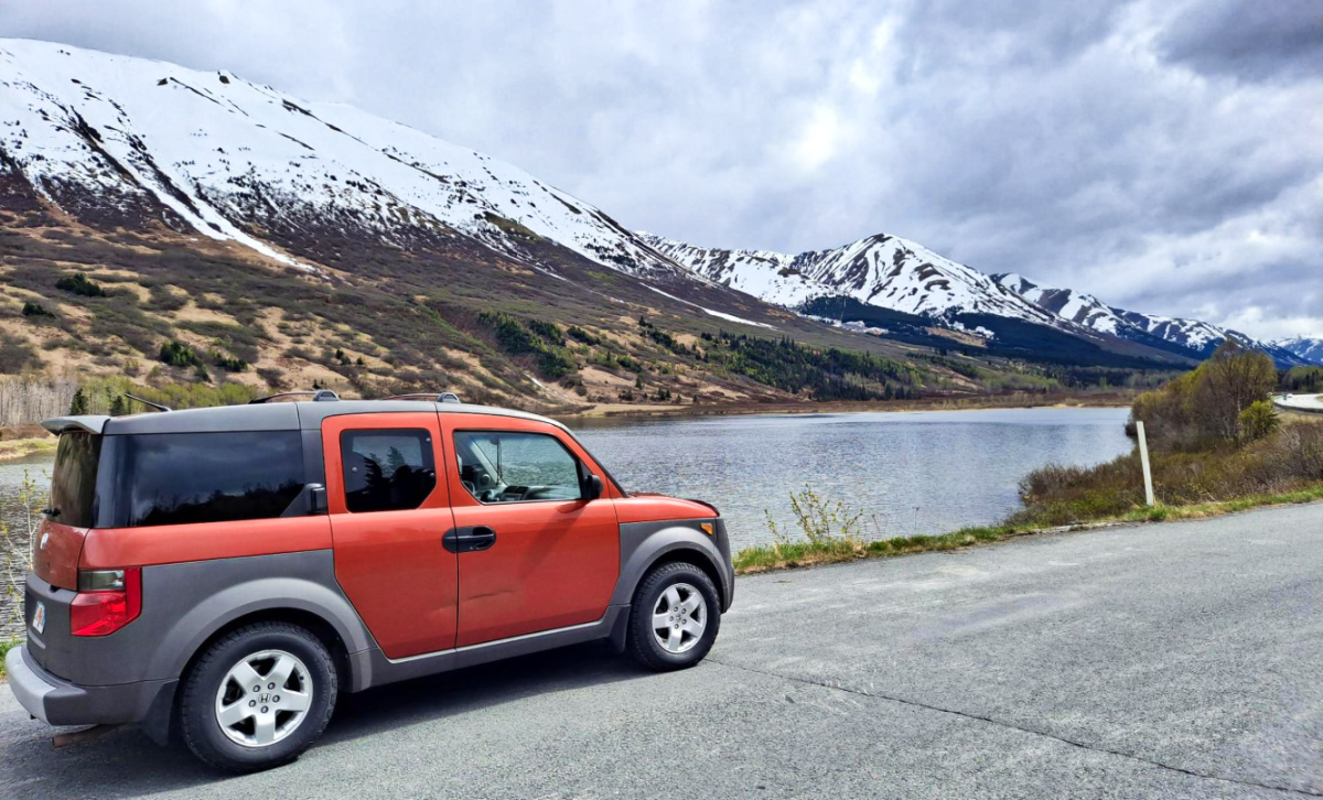 A red car driving with a scenic view of the snow covered mountain on Alaska’s Sterling Highway