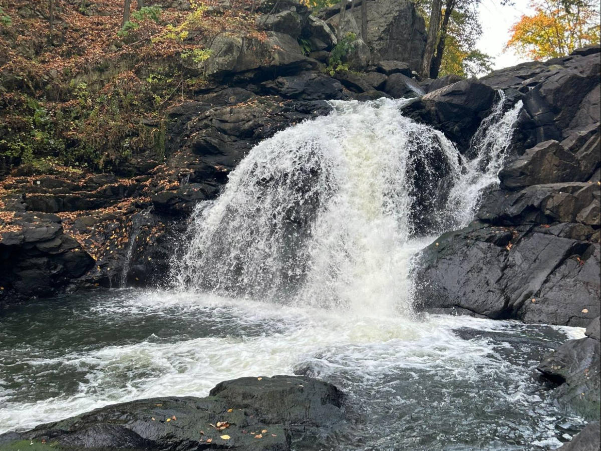 View of the fall foliage and huge rocks around the cascading water of Boonton Falls