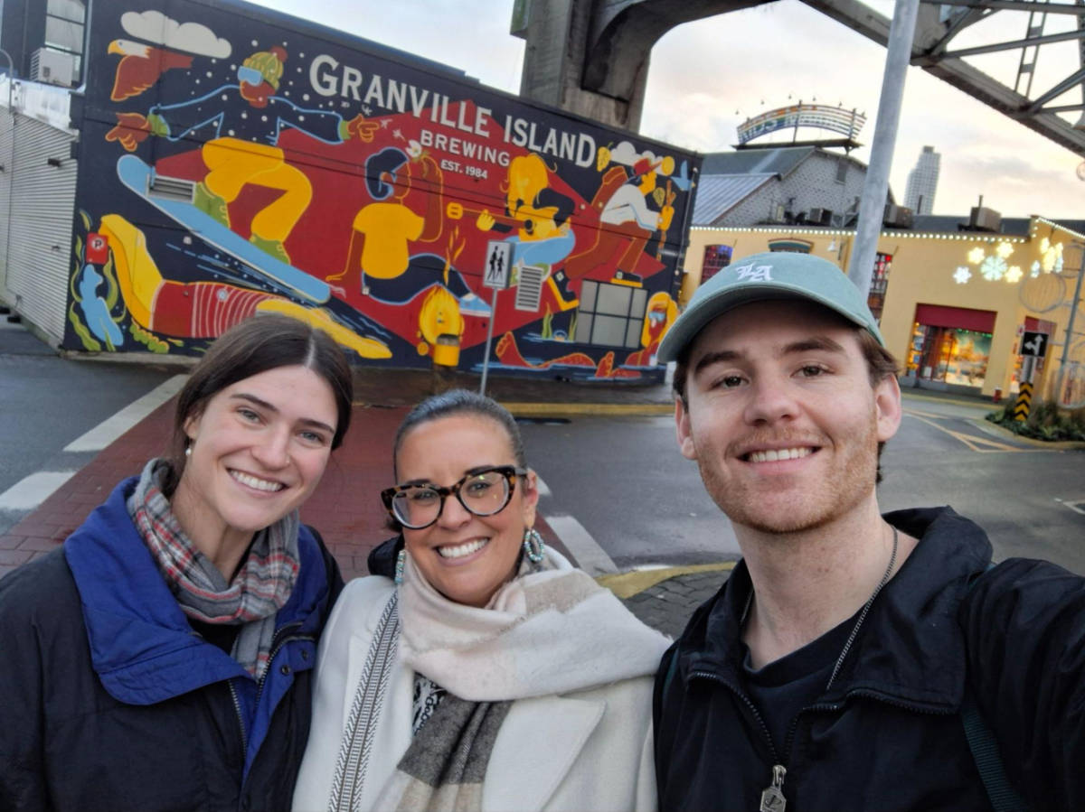 Travel Lemming writers Catherine and Betty with her partner Michael, smiling for a photo at the colorful mural in Granville Island