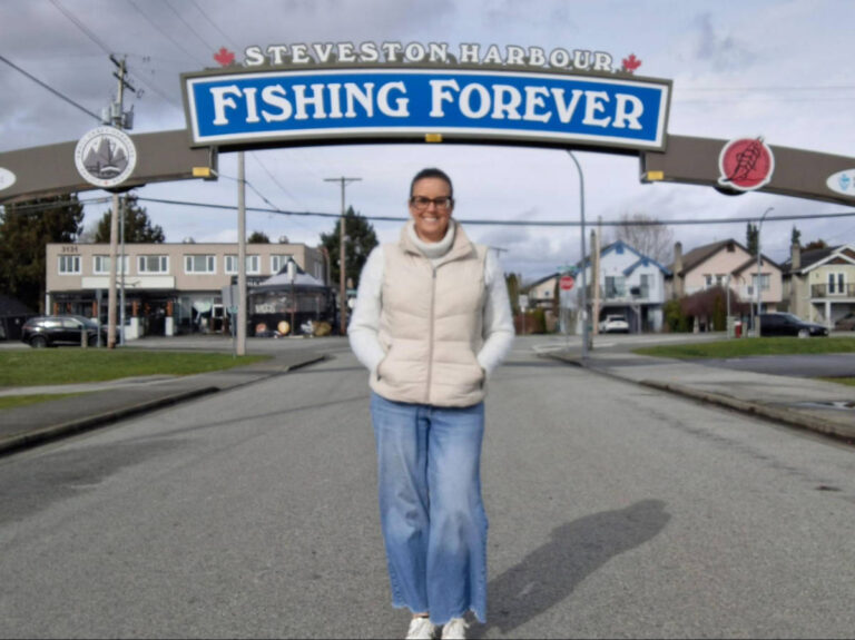 Travel Lemming writer Catherine Driver, smiling for a photo under the arch signage at the Steveston Harbour