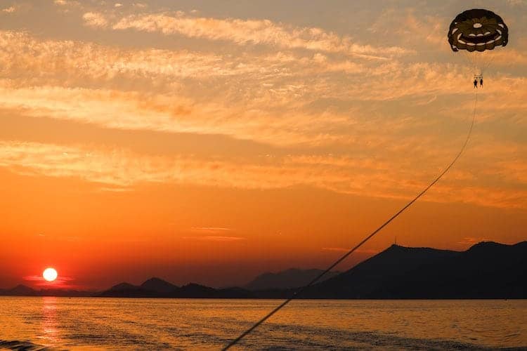Two people hang from a balloon while parasailing in Cavtat at sunset