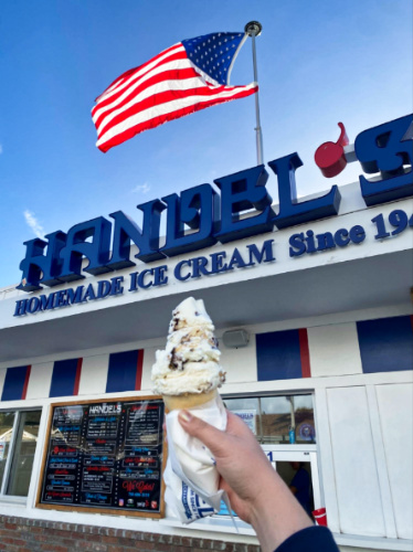 A hand holding a cheesecake oreo ice cream in front of the Handel’s Ice Cream with the USA flag on top