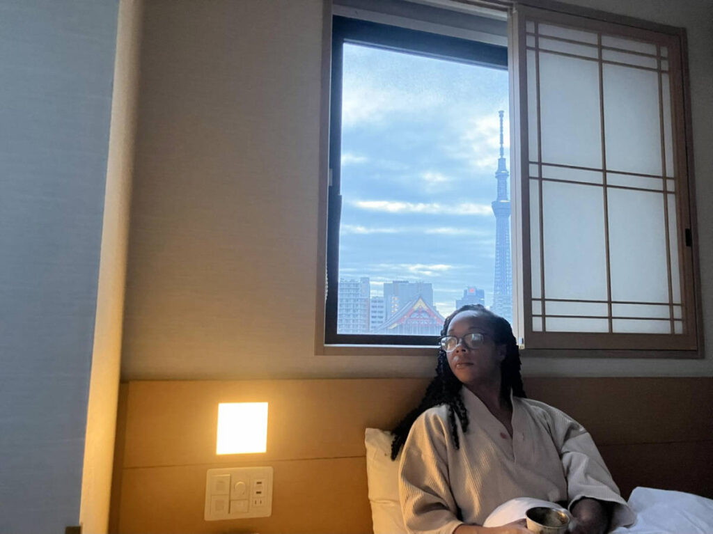 The author Chelsea Booker seating on their bed in their room at Onyado Nono Asakusa Natural Hot Spring