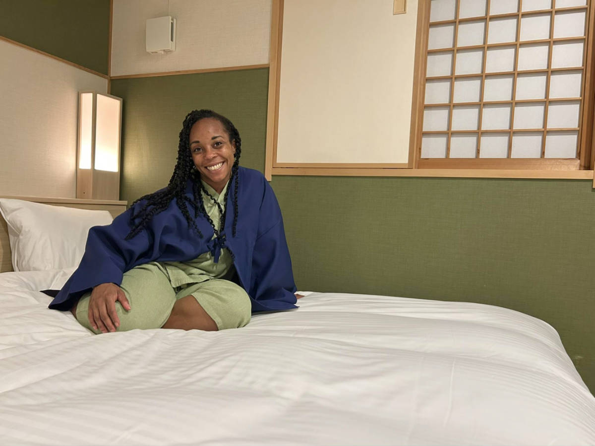 The author Chelsea Booker, smiling for a photo while sitting on the bed