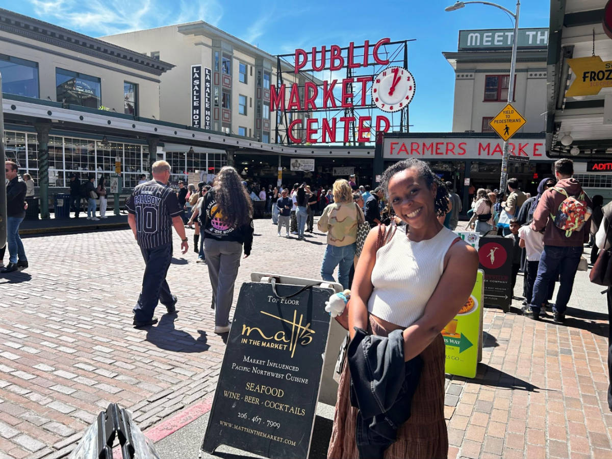The author Chelsea Booker, smiling in front of the entrance of Pike Place Market
