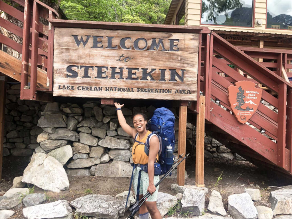 The author Chelsea Booker pointing the signage of Welcome to Stehekin