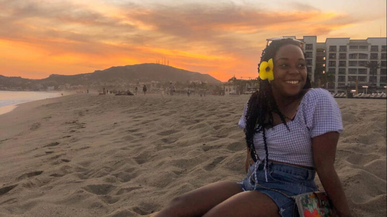 The author Chelsea Booker, smiling for a photo at the beach in Cabo San Lucas at sunset