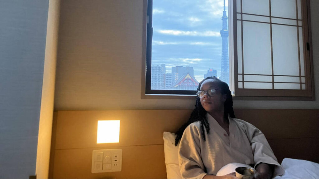 The author Chelsea Booker seating on their bed in their room at Onyado Nono Asakusa Natural Hot Spring
