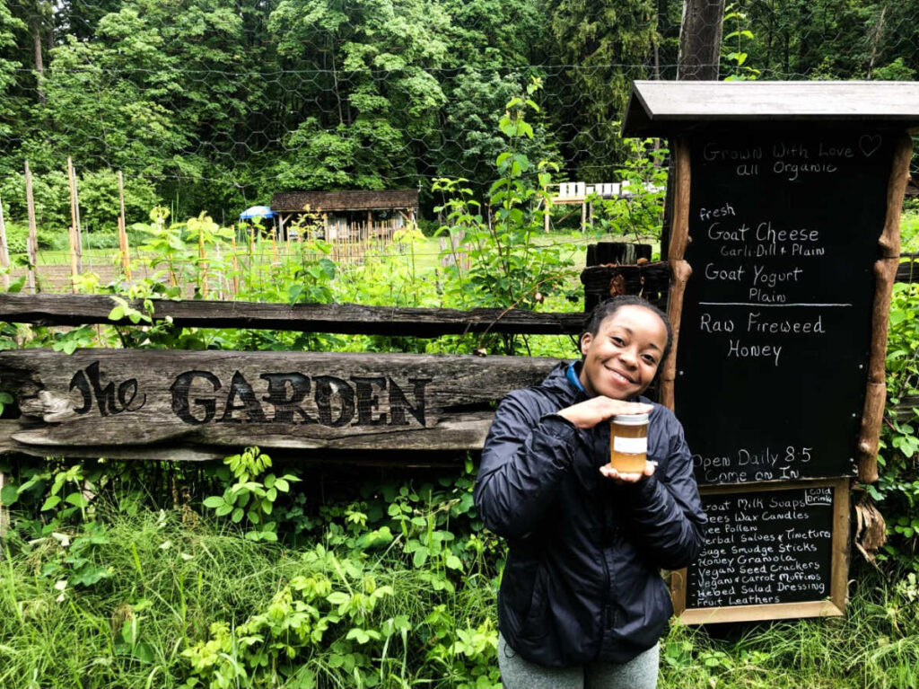 The author Chelsea Booker smiling for a photo while holding a  jar of honey at The Garden