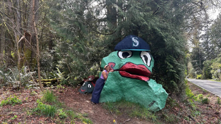 The author Chelsea Booker posing for a photo with the painted rocks of a frog and a lady bug in Bainbridge Island