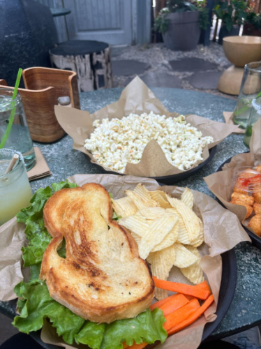 A plate of chicken salad sandwich with chips and another plate of popcorn at Greenhouse Bar