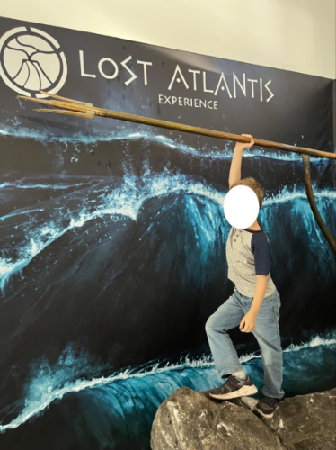 A kid posing in front of the poster of Lost Atlantis Experience