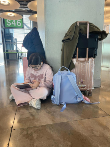 The author's daughter using a tablet while sitting on the floor at the airport in Madrid
