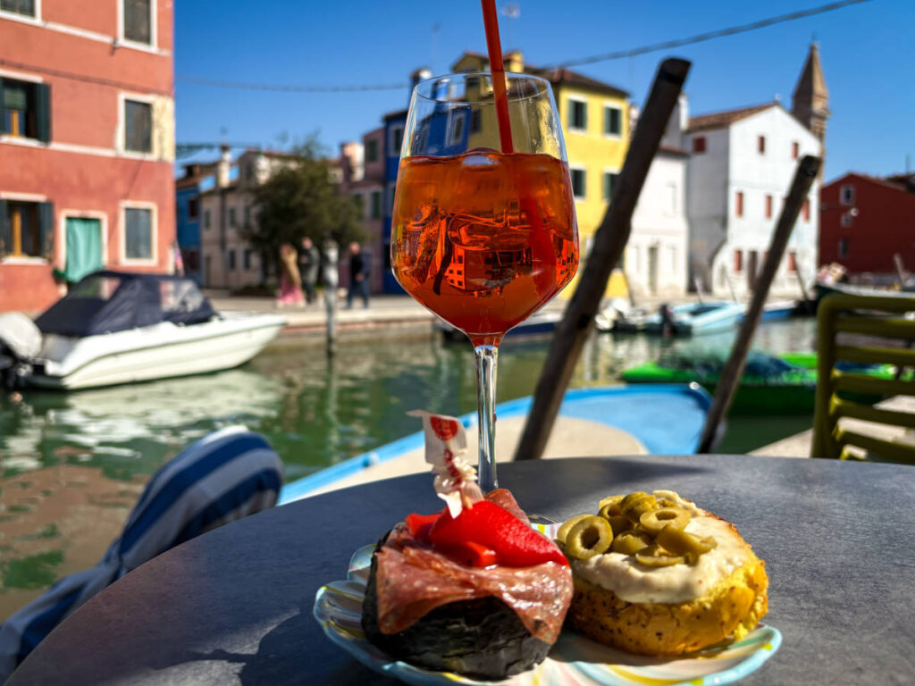 A plate of cicchetti and a glass of spritz by a canal in Burano