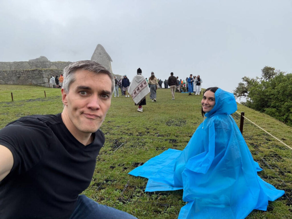 Travel Lemming Founder Nate Hake and Clara Kessler, sitting on the ground on a foggy and rainy day at Machu Picchu