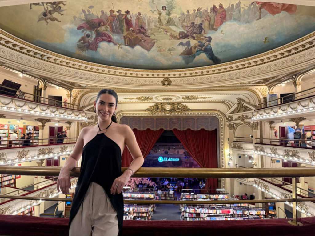 Travel Lemming writer Clara Kesseler, posing for a photo with an overlooking view of the book shelves and painted ceiling in El Ateneo Gran Splendid