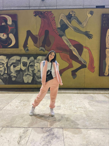 The author Claudicet Pena, posing for a photo in front of a mural at the airport