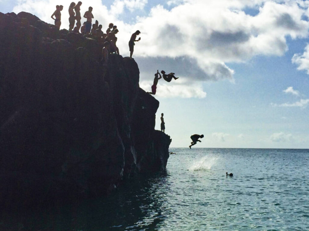 People cliff jumping at the “Da Big Rock” at Waimea Bay