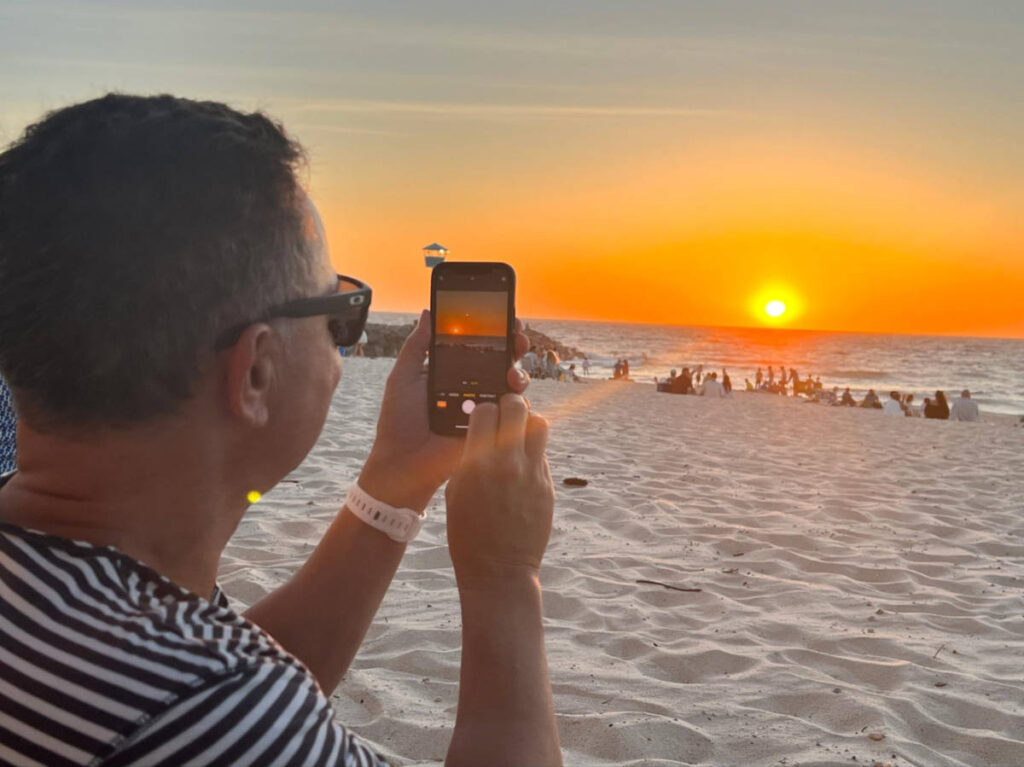 A man taking a photo of the sunset through his phone at Coastal Perth