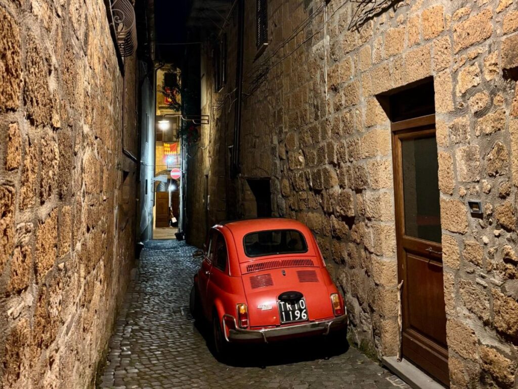 A small red car parked on a cobbled street at Orvieto