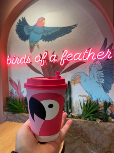 A hand holding a cup of coffee with the signage in the background