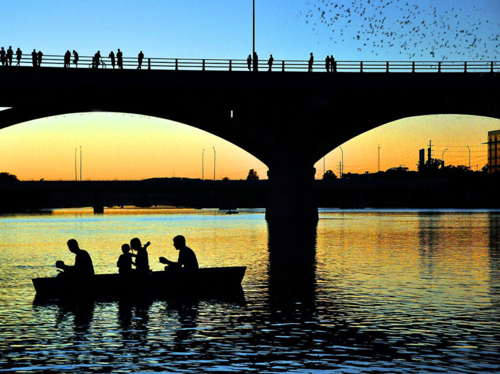 People standing at the Congress Avenue bridge and riding a small boat to watch the bats fly