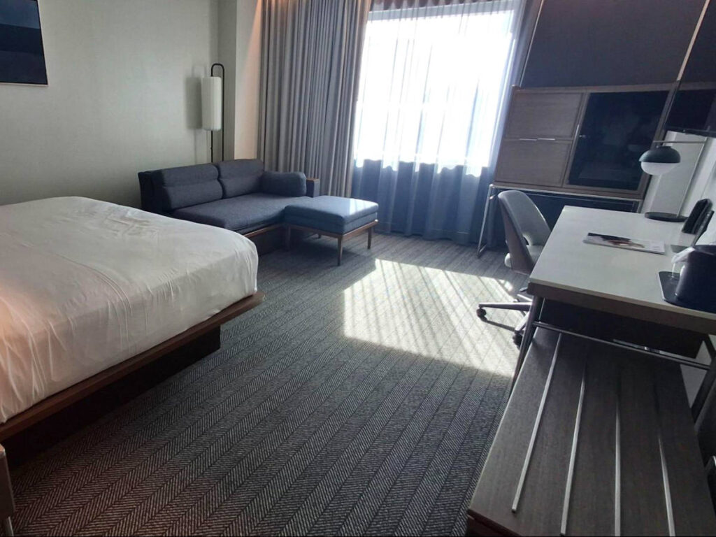 The bed, small sofa, and a large flat-screen TV above the desk