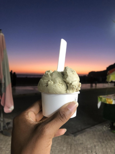 A hand holding a creamy gelato and a colorful sky on the background