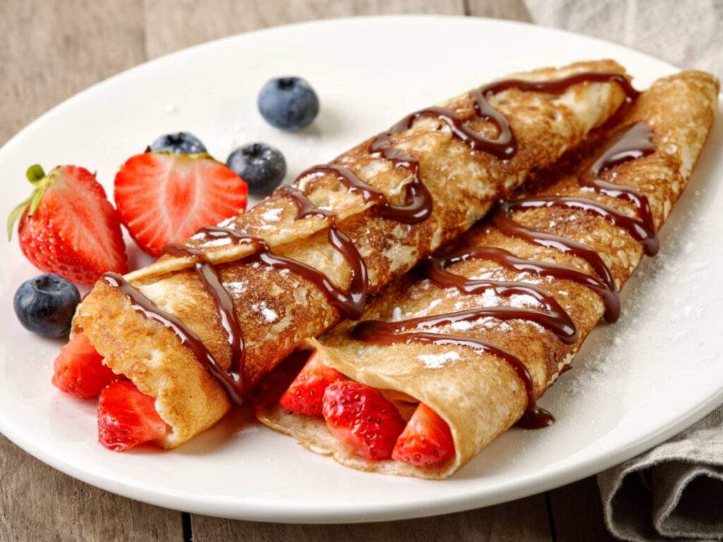 A plate of crepes with strawberries, blueberries and chocolate sauce