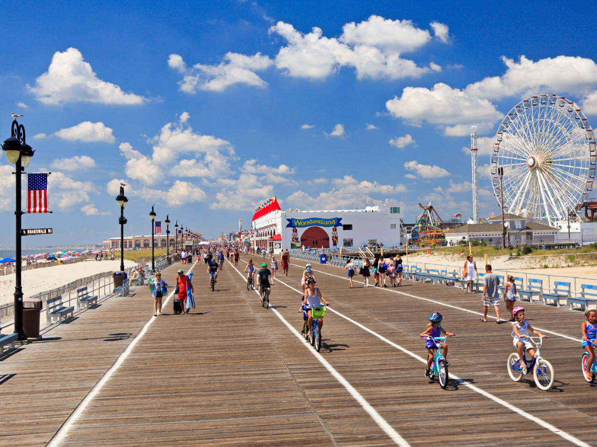 People walking and cycling along the boardwalk of Ocean City Beach on a sunny day