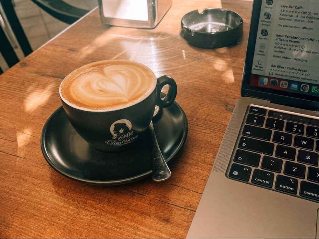 A cup of cappuccino beside a laptop