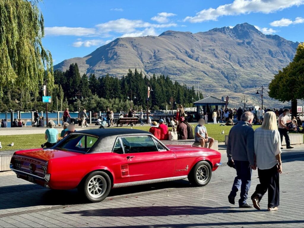 A red car parked and people relaxing in Downtown Queenstown