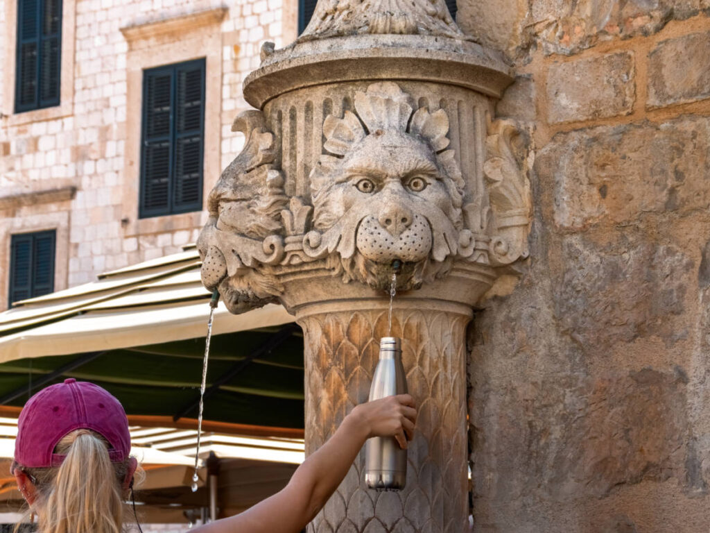 A woman refilling her water bottle from the lion sculpted water fountain in Dubrovnik’s Old Town
