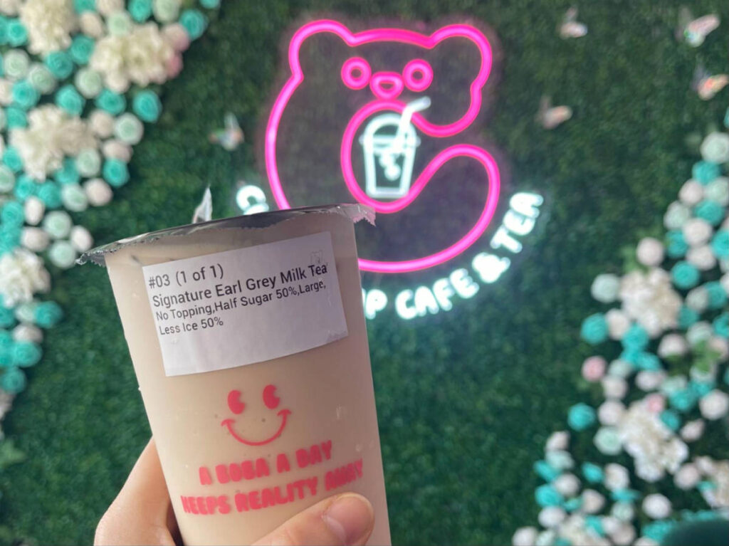 A cup of Earl Grey Milk Tea in front of a neon sign in Cuddle Cup Cafe & Tea