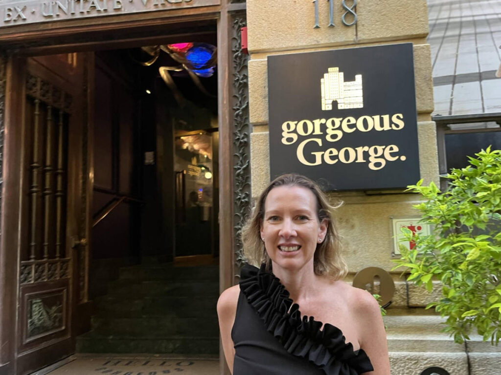The author Elise Kirsten, smiling for a photo at the entrance of Gorgeous George