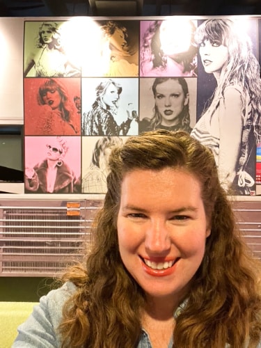 The author, Elizabeth Demolat, posing for a photo in front of Taylor Swift's poster at the Country Music Hall of Fame