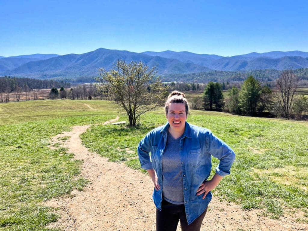 The author, Elizabeth, posing in the middle of the trail in Cades Cove Loop with a scenic mountain view in the background