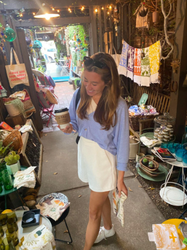 A woman in a blue shirt and white shorts holding a coffee at Fig Curated Living