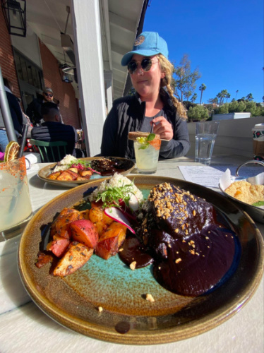 Author Jess Levy sitting at a outdoor table with a plate of food, including chicken mole and popsicle cocktails at Cocina Barrio