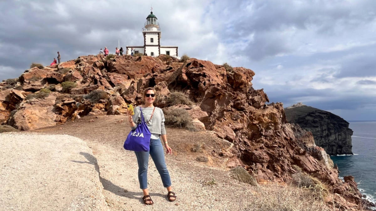 The author Erin Henk, smiling with the view of the Akrotiri Lighthouse in Santorini