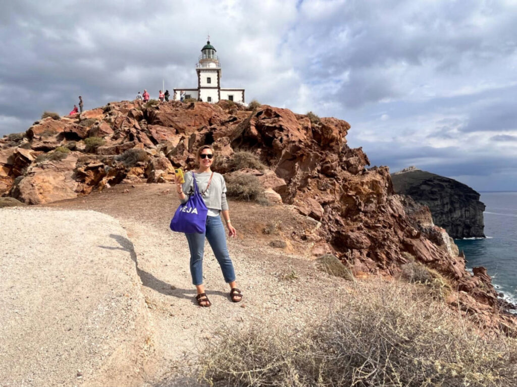The author Erin Henk, smiling with the view of the Akrotiri Lighthouse in Santorini
