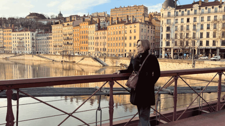 The author Erin Henk, posing for a photo with a panoramic view of the Old City on the Passarelle Saint-Vincent