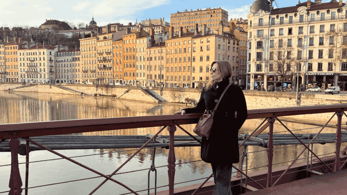 The author Erin Henk, posing for a photo with a panoramic view of the Old City on the Passarelle Saint-Vincent