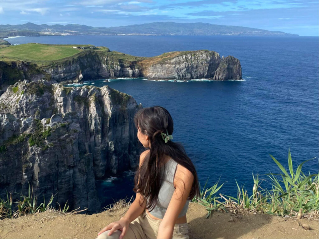 Author Lea Rose Allbaugh sitting on a rock, gazing at the ocean on Sao Miguel Island