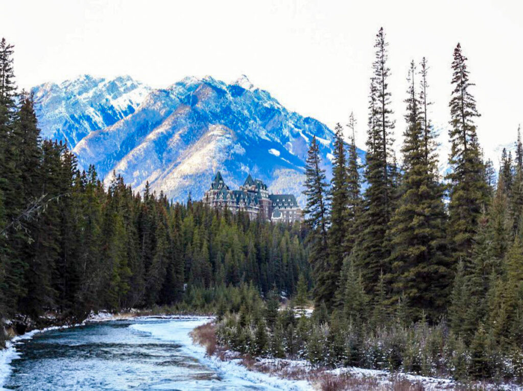 Banff Springs Hotel against a background of the Canadian Rocky Mountains with trees and a river in the foreground