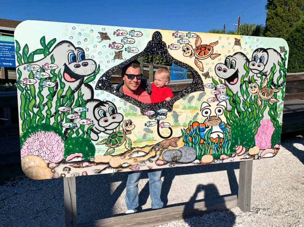 A father and son, smiling for a photo behind the cutout sign at TECO Manatee Viewing Center