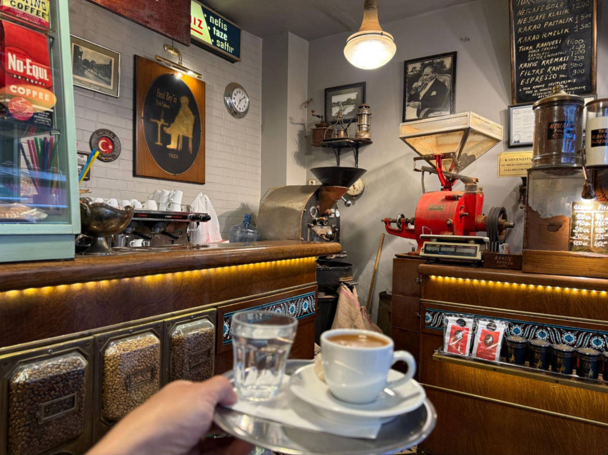A hand holding a tray with coffee and a glass of water at Fazil Bey's Turkish Coffee