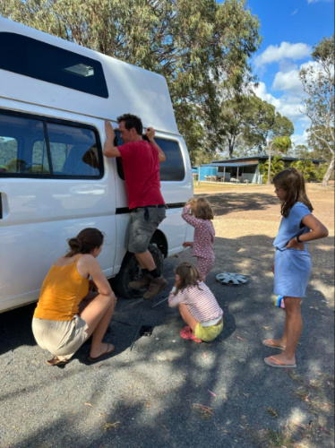 A man fixing the flat tire while the girls watch him